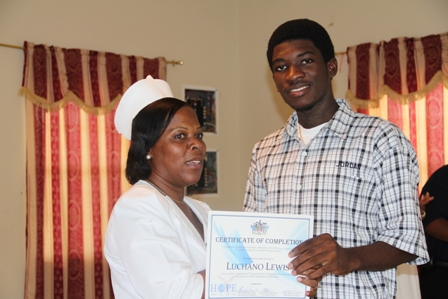 (L-R) Charlestown Secondary School student Mr. Luchano Lewis one of the 50 interns receives his certificate of completion in the 8th Annual Summer Job Attachment Programme from Health Services Coordinator and Head Nurse at the Alexandra Hospital Mrs. Aldris Pemberton