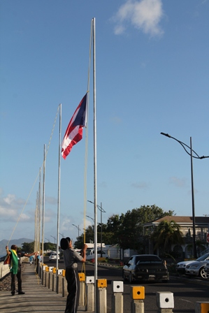 An officer of the Royal St. Christopher and Nevis Police Force hoisting the flags at the Charlestown Waterfront on February 14, 2014. He is assisted by Devon Liburd Director of Sales and Marketing at the Nevis Tourism Authority