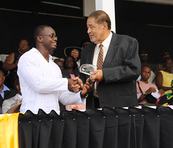 Didier Rohan receives an award on behalf of Lornette Manners from His Honour Eustace John Deputy Governor General for her services in Education