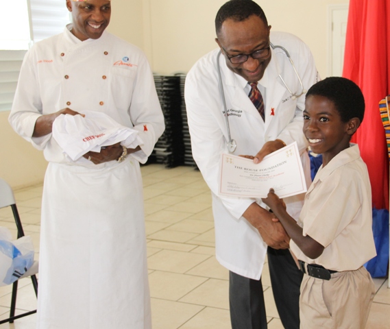 Head of the Rouse Foundation, Cardiologist Dr. Charlie Rouse and Celebrity Chef of Atlanta Marvin Woods, distribute Certificates of Participation and chef gear to students of the Charlestown Primary School for their participation in the Mini Chef Academy on February 24, 2015  