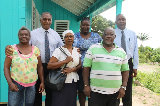 (L-r back row) Premier of Nevis Hon. Vance Amory flanked Pearl Smithen mother of Vanessa (extreme left), Cabinet Secretary in the Nevis Island Administration Stedmond Tross, (front row), Ms. Glorita Vaughn, Community Caregiver in the Ministry of Social Development, Senior Citizens Division responsible for Gingerland and contractor Phillip Walters standing on the doorsteps of a new home given to Vanessa Smithen (back row second from right) on June 24, 2016 by the administration