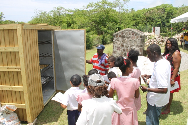 Students of the Montessori Academy Nevis with Principal Denis Morgan, tour guide John Hanley, Acting Permanent Secretary in the Ministry of Tourism and the baker Oliver “Powers” Liburd experiencing what life was like in Nevis at the Nevisian Heritage Village during the Ministry of Tourism’s Open Day, a part of Exposition Nevis on May 11, 2017