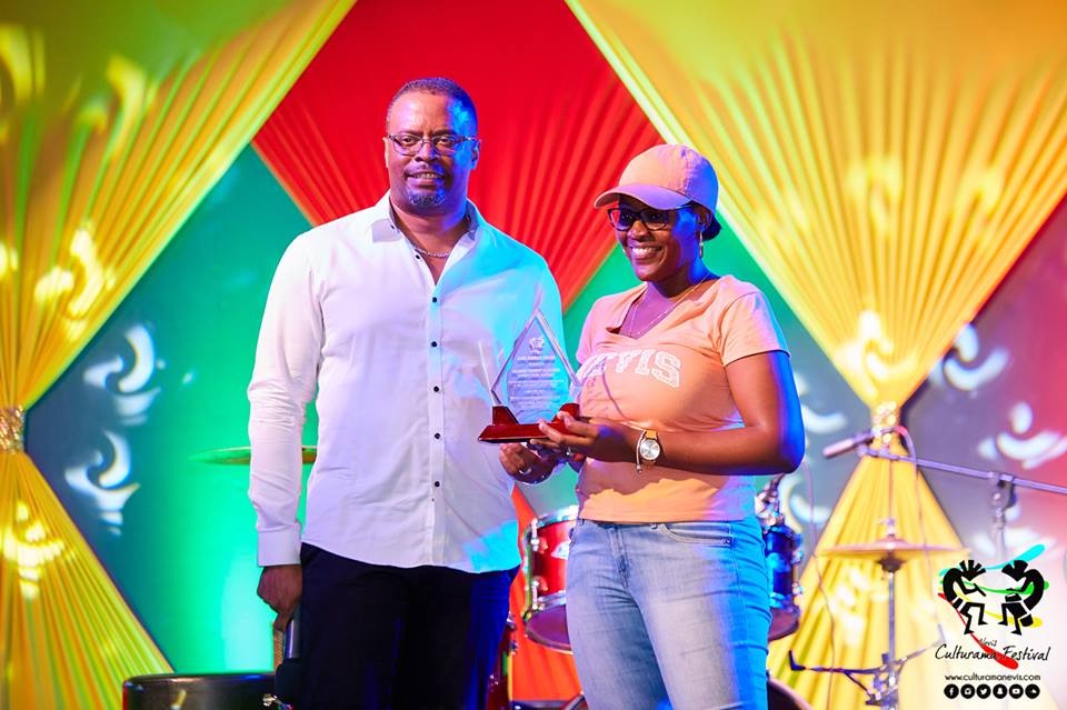 Hon. Mark Brantley, Deputy Premier of Nevis and Minister of Culture presents token of appreciation to Chevaughn Claxton on behalf of her father Oldain “Sandy” Claxton on July 04, 2017, for his long standing contributions at the Cultural Village