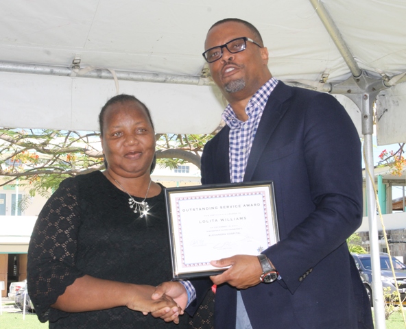 Minister of Health Hon. Mark Brantley, presents a certificate of recognition to Mrs. Ermine Jeffers, Coordinator of the Community Nursing Services on behalf of the Public Health Unit, at the hospital’s Pre-Christmas Programme on December 13, 2017, for their outstanding performance in 2017