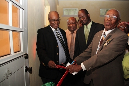 (Extreme right) Renowned Combermere Villager Mr. Franklyn Browne cuts the ribbon at the official opening of the Combermmere Community Centre. Looking on are (L-R) Premier of Nevis hon. Joseph Parry, Minister for Social Development on Nevis Hon. Hensley Daniel Daniel, Area Representative, Attorney General of St. Kitts and Nevis and Federal Minister of Legal Affairs Hon. Patrice Nisbett. Back row (L-R) Minister of Trade on Nevis Hon. Dwight Cozier and a Villager