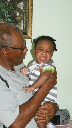 NevCan Cultural Association’s Vice President Mr. Hugh Jeffers visits with baby K’yun Elliott at his home in Stoneygrove shortly after his grandmother Ms. Rodney Elliott was presented with financial assistance to help defray cost of medical expenses when he was newly born