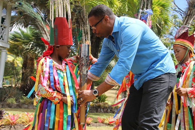 Deputy Premier and Minister of Culture, Hon. Mark Brantley, passes the Queen’s Baton to a Nevisian masquerade dancer