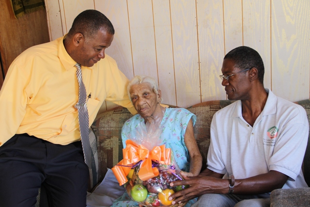 Federica France a retiree from the Department of Agriculture on Nevis being presented with a fruit basket as a token of appreciation from the Department and Ministry of Agriculture on May 21, 2014, by Director of Agriculture Keithley Amory (right) and Permanent Secretary in the Ministry of Agriculture Eric Evelyn (left) at her home in Camps, as part of Agriculture Awareness Month