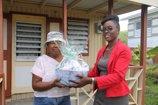 Director of the Nevis Investment Promotion Agency Kimone Moving presents a gift basket from NIPA and the Nevis Financial Services Department to Govanie Ward for her mother Selena Ward in Camps, who is the oldest person in the St. James’ Parish