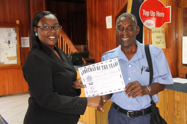 Deputy Post Mistress General Rhonda Forbes-Williams presents “Postman of the Year” award for 2014 to Vernon “Tim” Wilkinson at the Post Office in Charlestown