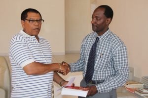Chairman of The Combermere Reunion Committee Rumelo Jeffers presenting Assistant Secretary in the Premiers Ministry Kevin Barrett, with the books donated by Vincent Joseph, during a handing over ceremony held at the Franklyn Browne Community Centre on July 29, 2015