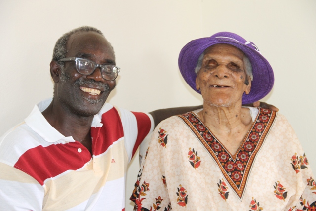 Centenarian Eileen Swanston Smithen with her adopted son and caretaker Pastor Theophilus Kelly, moments after she received a royal birthday card from Her Majesty Queen Elizabeth II on the occasion of her 100th birthday from Governor General of St. Kitts and Nevis His Excellency Sir Tapley Seaton at her home in Zion Village on July 13, 2017