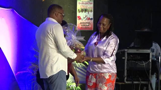 Deputy Premier of Nevis Hon. Mark Brantley presenting a fruit basket to Mrs. Garcia Hendrickson, outgoing Coordinator of the Department of Social Services Senior’s Division in the Ministry of Social Development, at the Miss Nevis Senior Pageant at the Nevis Cultural Complex on October 28, 2017