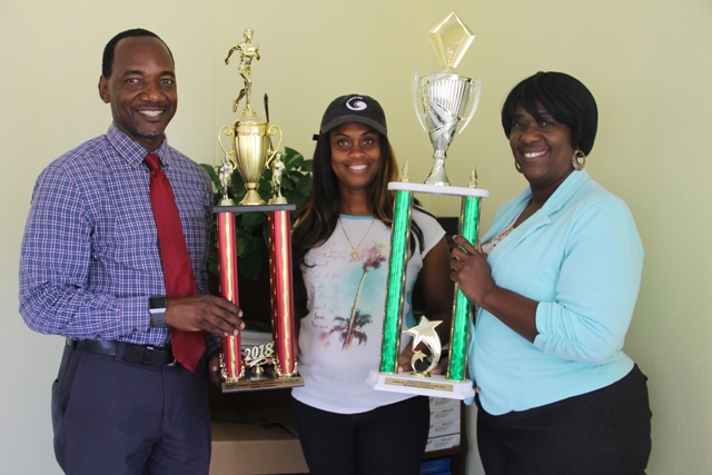 Mr. Kevin Barrett, Permanent Secretary in the Ministry of Education and Library Services (left) and Mrs. Terres Dore, Education Officer (right) presenting winning trophies to Ms. Latoya Jeffers, Principal of the Charlestown Primary School, winners of the 2018 Gulf Insurance Inter-primary Schools Athletics Championship on April 05, 2018, at the Ministry of Education at Marion Heights