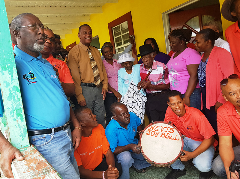 (l-r top row) Mr. Abonaty Liburd, Executive Director of the Culturama Secretariat. Mr. Jerome Rawlins, Chief Executive Officer of the Nevis Cultural Development Foundation, Hon. Eric Evelyn Minister of Culture and other staff of the Nevis Cultural Development Foundation visiting Cultural icon Mr. David Freeman (fourth from right) on his 90th birthday on February 16, 2018, at his home in Gingerland with Mrs. Clarestine Freeman (fifth from right), his wife standing beside him