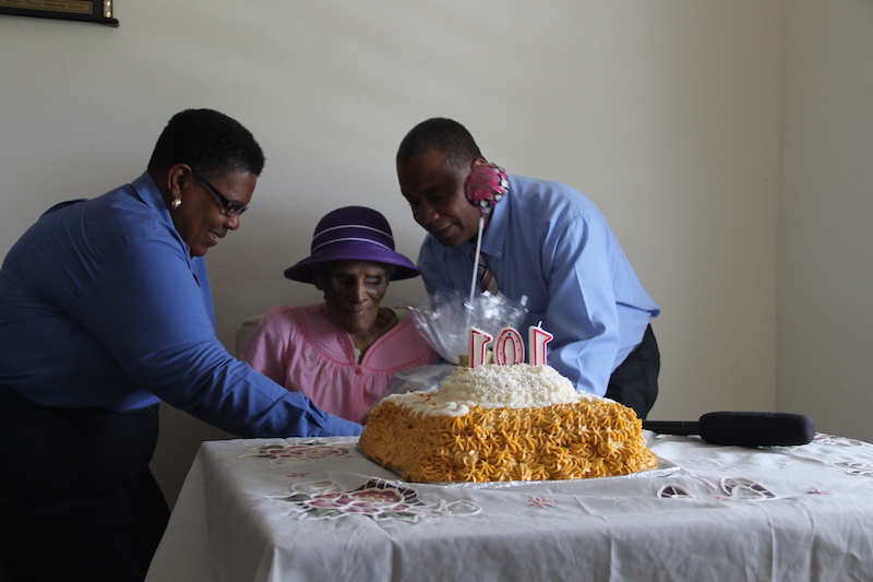 Ms. Ilene Smithen receives her gift basket from Hon. Eric Evelyn, Minister responsible for the Ministry of Community Development, with the assistance of Ms. Joyce Moven, Deputy Director at the Department of Social Services at her 101st birthday celebration at her home on June 20, 2018