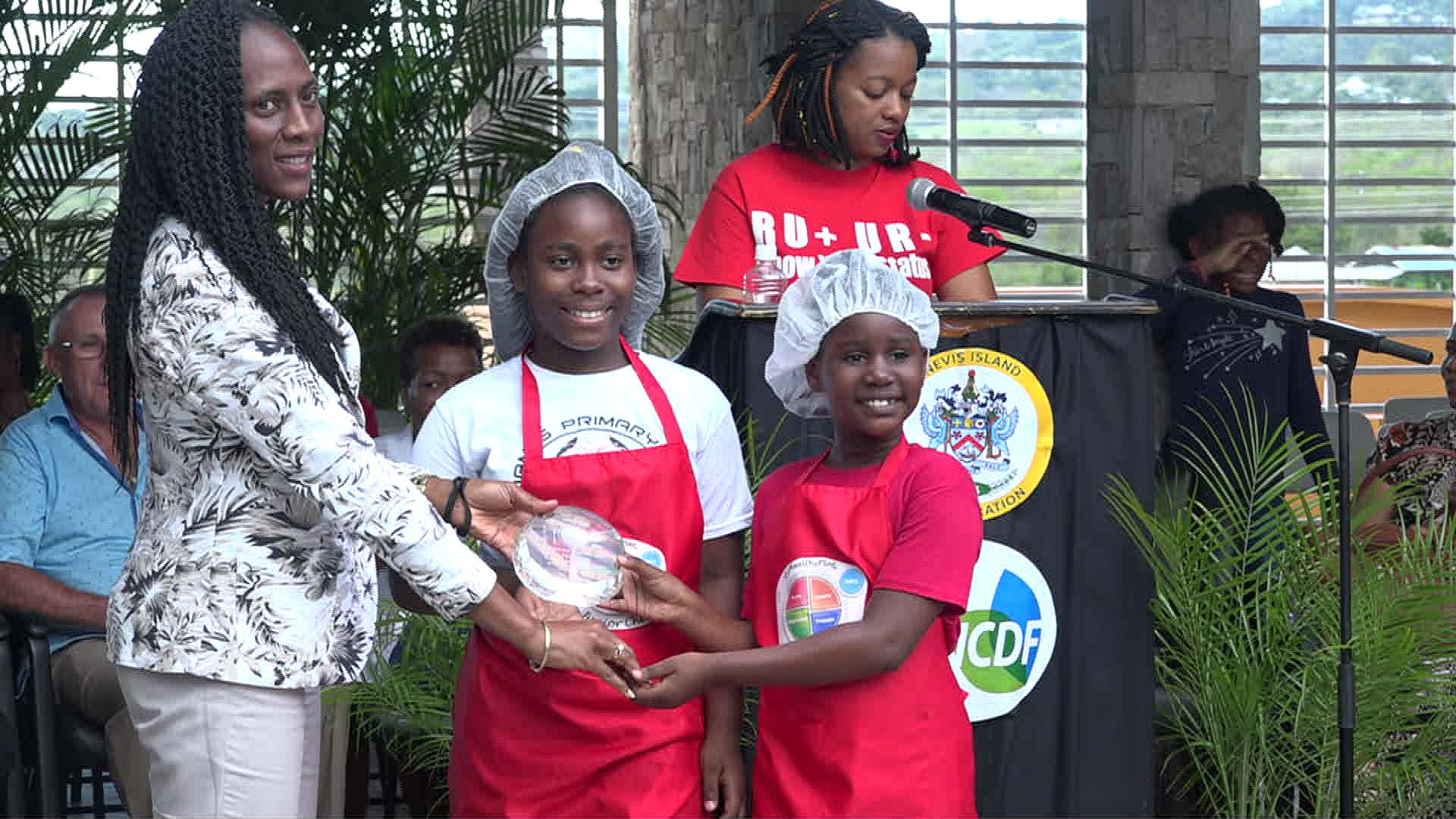 Mrs. Shelisa Martin-Clarke Acting Permanent Secretary in the Ministry of Health presents a trophy to joint 1st place winners in the MyHealthyPlate Junior Chef Competition, to Ms. La-Taivia Powell and Ms. Alicia Wallace of the St. James Primary School, at the Nevis Performing Arts Centre courtyard on April 15, 2019