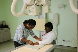 Mrs. Karema David, Radiographer at the Alexandra Hospital preparing Hon. Hazel Brandy-Williams, Junior Minister of Health to take an x-ray of her hand during the official commissioning of the new Direct Radiography system at the E-Ray Unit on October 11, 2019