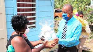 Hon Eric Evelyn presenting a gift basket to Mrs. Denise Browne for her 103 year-old mother-in-law Mrs. Mary Brown of River Path, on behalf of the Ministry of Social Services and the people of Gingerland in observance of Centenarians Day celebrated on May 31, 2020