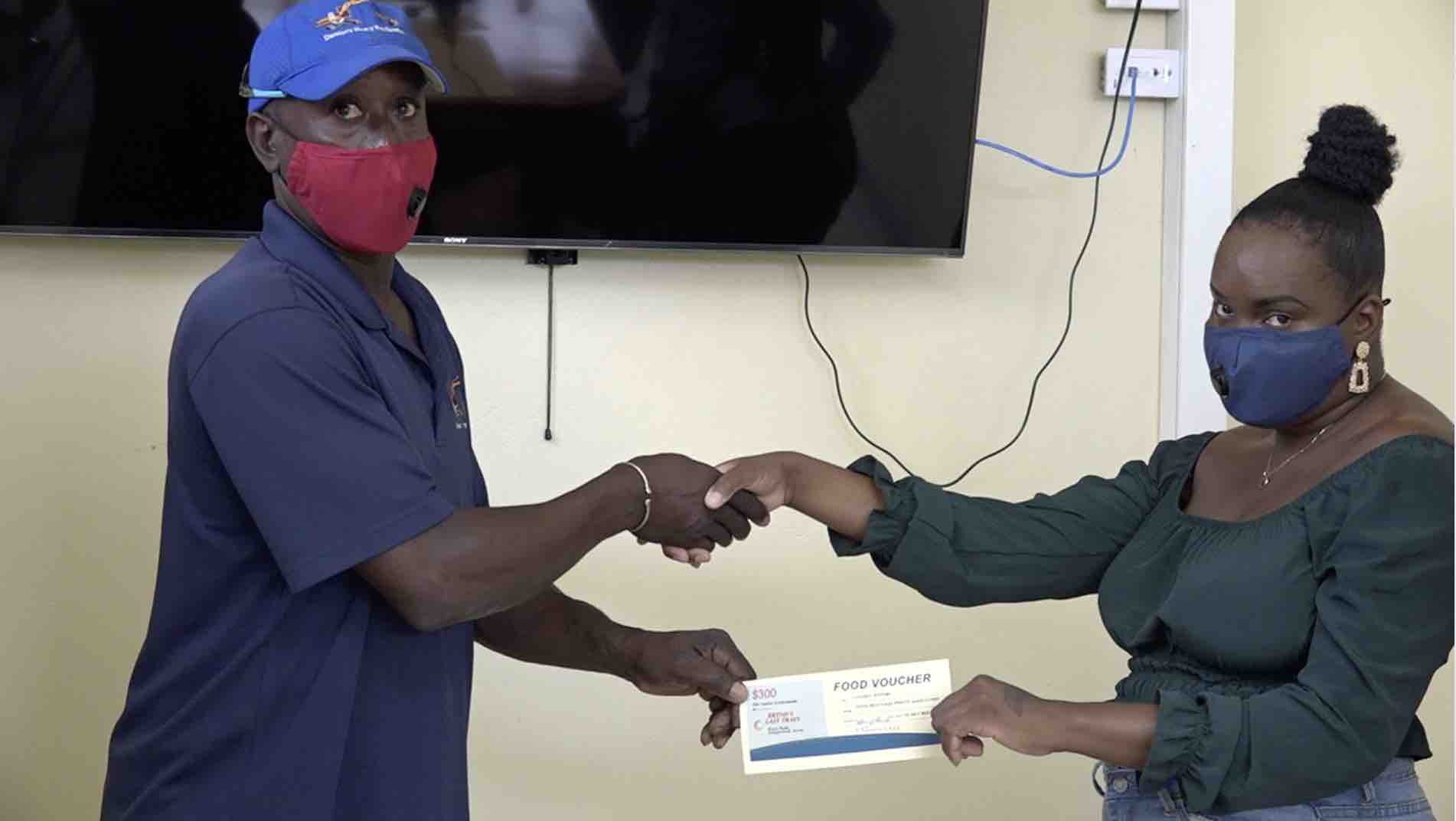 Mr. Duncan Mills, representing the truckers and heavy equipment operators working with the Public Works Department, presents a $300 food voucher Ms. Natasha Jeffers, a young other on Nevis on June 29, 2020