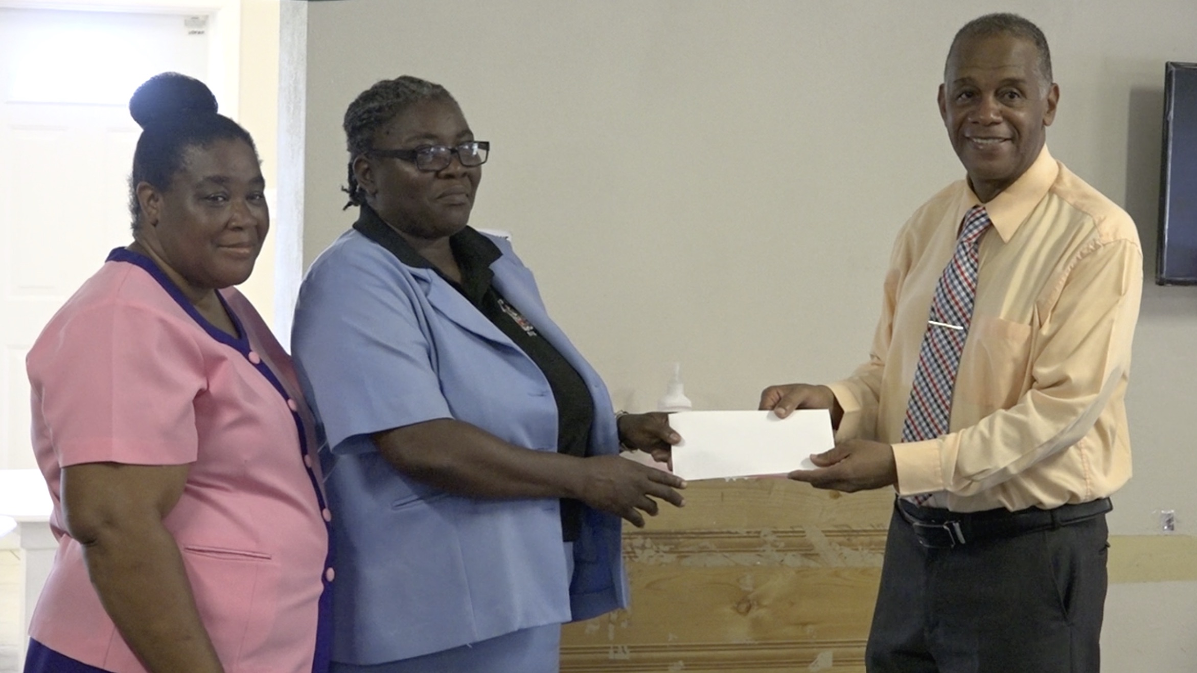 Hon. Eric Evelyn, Minister of Youth, Community Development, and Area Representative for St. George’s Gingerland presenting a financial donation to Ms. Dawnny Lanns, Education Officer responsible for the Gingerland Preschool on behalf of the school on October 09, 2020. Ms. Pamela Elliott, Supervisor of the Gingerland Preschool looks on