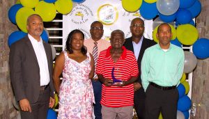 (L-r) Hon. Spencer Brand, Minister of Water Services on Nevis; Ms. Tonya Bartlette, Manager of the Nevis Water Department; Mr. Denzil Stanley, Principal Assistant Secretary in the Ministry of Water Services; Mr. Conrad “Monks” Huggins honoured on his retirement from the Nevis Water Department; Dr. Ernie Stapleton, Permanent Secretary in the Ministry of Water Services; and Mr. Roger Hanley, Operation Manager at the Nevis Water Department during a Retirement Cocktail celebration at the Nevis Performing Arts Centre on September 30, 2021