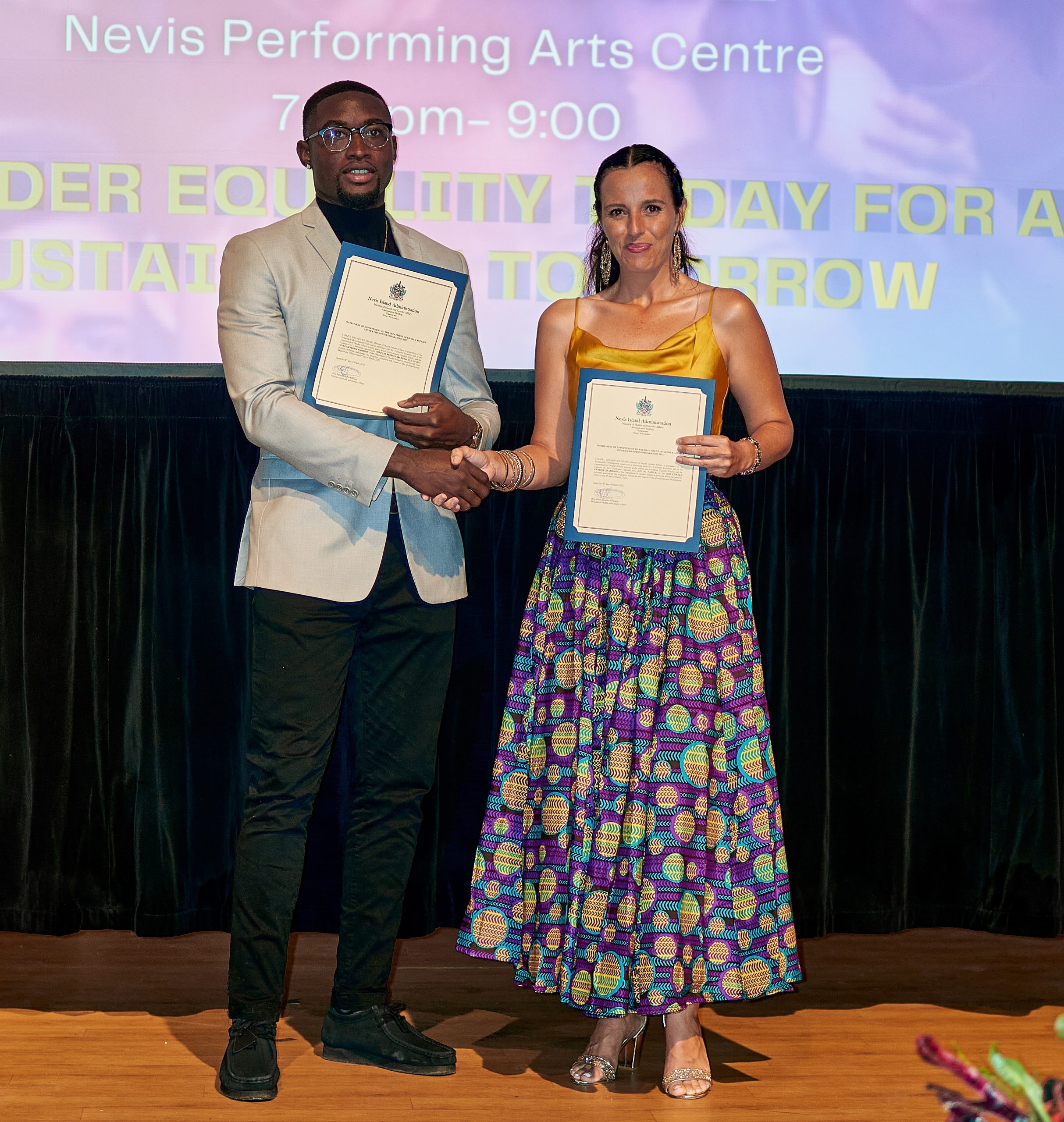 (l-r) Mr. Colin Kezron Archibald and Ms. Joy Napier, the first gender champions in the Department of Gender Affairs’ Gender Champions Programme, showing off their Instruments of Appointment at the Ministry of Health and Gender Affairs’ International Women’s Day Awards Ceremony at the Nevis Performing Arts Centre on March 08, 2022