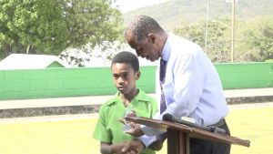 Hon. Eric Evelyn, Minister of Youth and Area Representative for the St. Georges’ Parish, presents award to Ziondre Dore of Joycelyn Liburd Primary School in observance of International Day of the Boy Child 2022