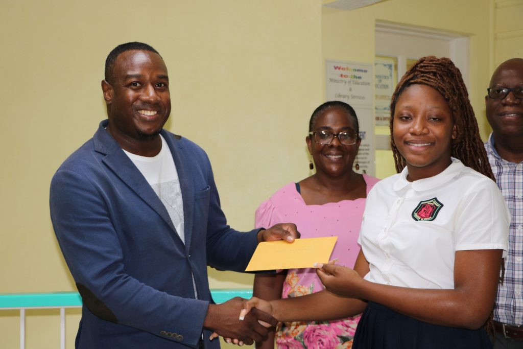 Mr. Eustace Theo Wallace of Hamilton, Minister-Counselor at the St. Kitts and Nevis High Commission to Canada, presenting Ms. Shadé Bridgeman, a student of the Charlestown Secondary School with a Wallace Family Bursary at a handing over ceremony at the Department of Education on August 30, 2022, with Ms. Angela Monzac, Head at the Modern Languages Department at the school; and Principal Mr. Juan Williams looking on