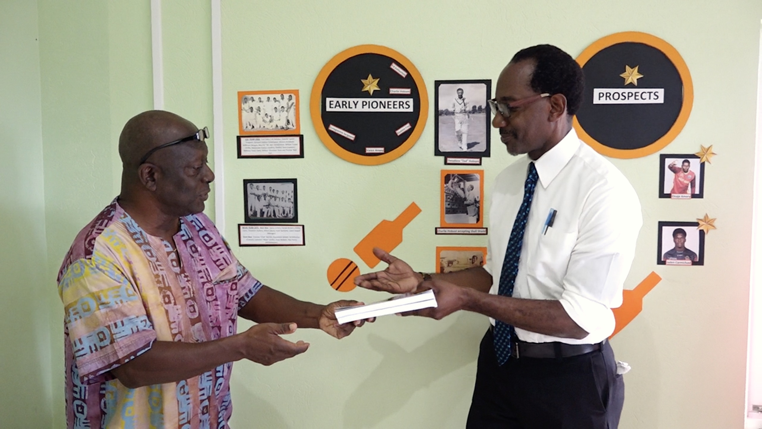Mr. Stevenson Manners presenting Mr. Kevin Barrett, Permanent Secretary in the Ministry of Education, Library Services, Youth and Sports on Nevis with two copies of his book entitled “The Father Son and Offsprings” for the Nevis Library Services and the Nevis Sports Museum recently at an exhibition at the library in Charlestown