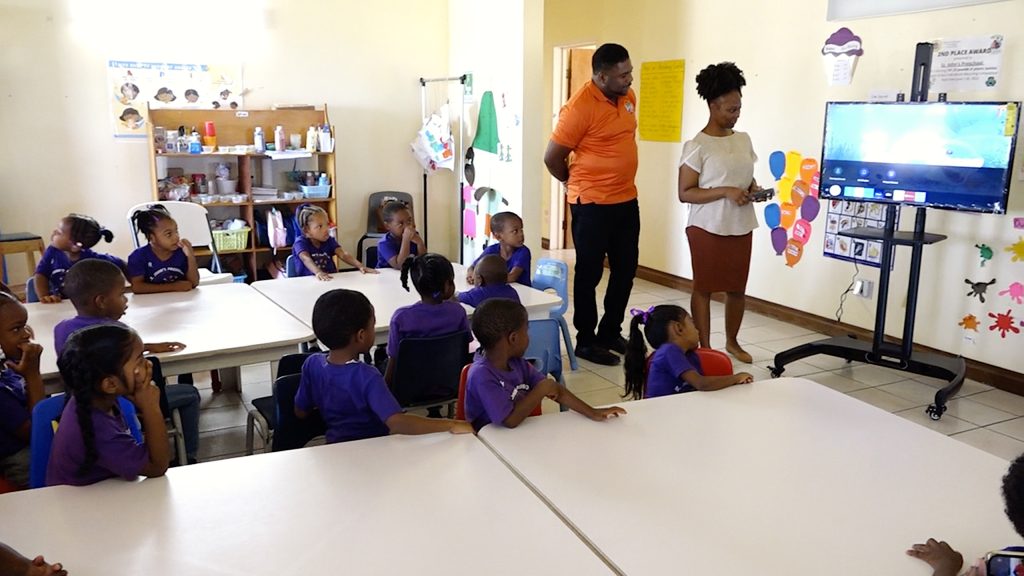Hon. Troy Liburd, Minister of Education on Nevis, moments after presenting a 42-inch Samsung smart television on mobile stand to Ms. Winette Hobson, Supervisor of the St. John’s Preschool on February 10, 2023, while students look on