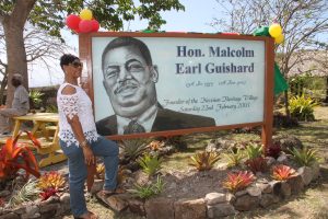Mrs. Yvonne Guishard with a portrait of her husband the late Hon. Malcolm Guishard former Minister of Tourism and Culture erected at the Nevisian Heritage Village in Gingerland by the Ministry of Tourism for the establishment of the facility on its 15th anniversary in 2018 (file photo)